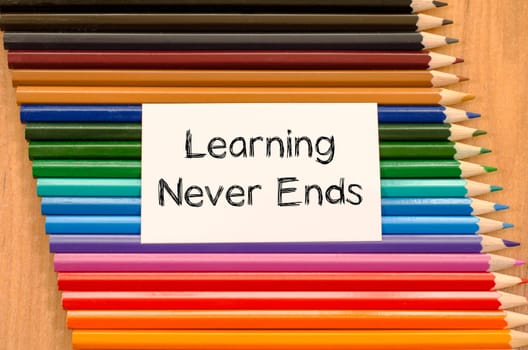 Learning never ends text concept and colored pencil on wooden background