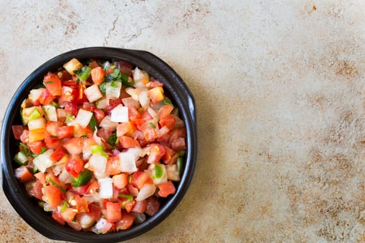 Bowl of fresh pico de gallo on stone surface with copy space and viewed from above.