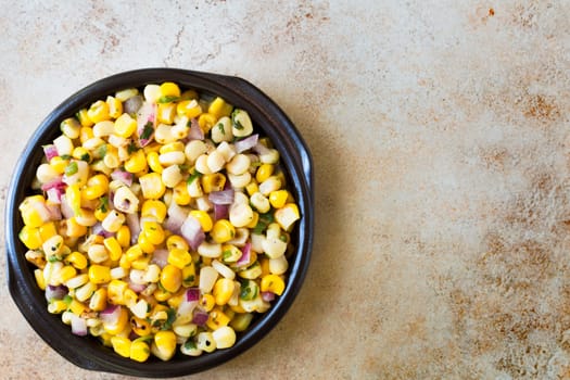 Bowl of fresh grilled corn salsa on stone surface with copy space and viewed from above.