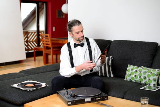 young man in white shirt with bow-tie with old records in his living room