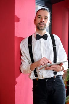 young bearded man in white shirt with bow-tie with teblet PC
