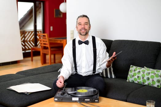 young man in white shirt with bow-tie with old records in his living room