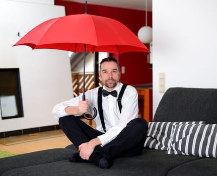 man in white shirt with bow-tie sitting in the living room with umbrella