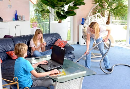 boy playing with computer,his sister using smartphone at home and mother doing homework