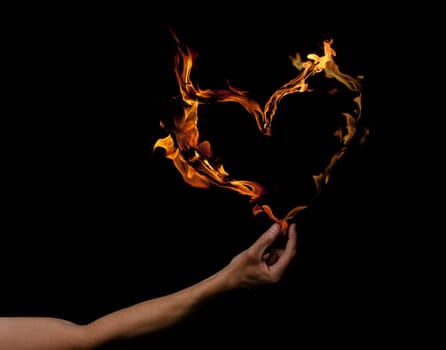 Hand holding heart shaped flames on a dark background
