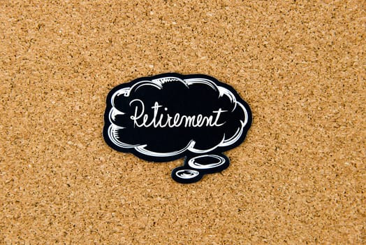 RETIREMENT written on black thinking bubble over cork board background, copy space available