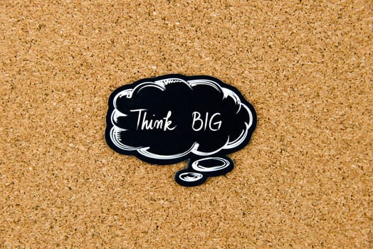 Think BIG written on black thinking bubble over cork board background, copy space available
