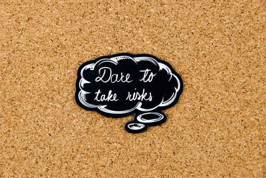 DARE TO TAKE RISKS written on black thinking bubble over cork board background, copy space available