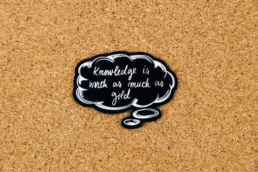 KNOWLEDGE IS WORTH AS MUCH AS GOLD written on black thinking bubble over cork board background, copy space available