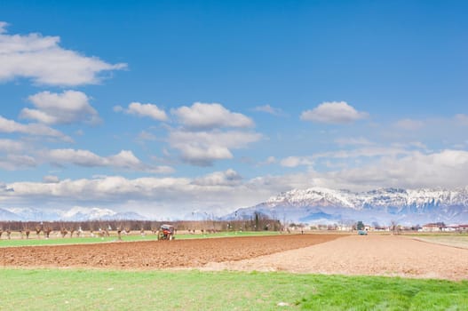 Agricultural landscape. With tractor plow a field. The mountains in the background.