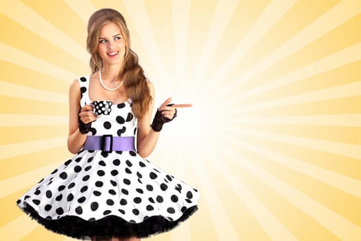 Creative vintage photo of a beautiful pin-up girl in a polka dot dress, holding a cup of tea and pointing aside on colorful abstract cartoon style background.