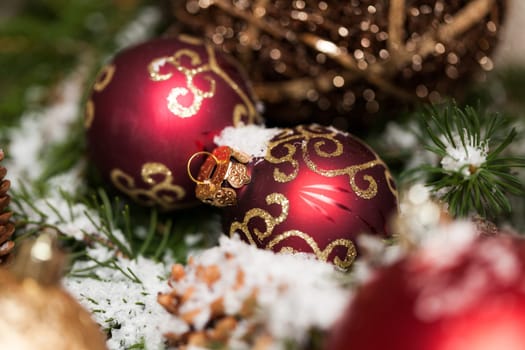red Christmas baubles between cones and fir branches covered with snow as macro detail
