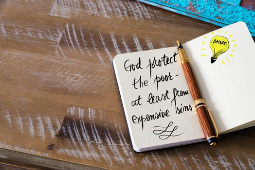 Handwritten text God protect the poor — at least from expensive sins with fountain pen on notebook. Concept image with copy space available.