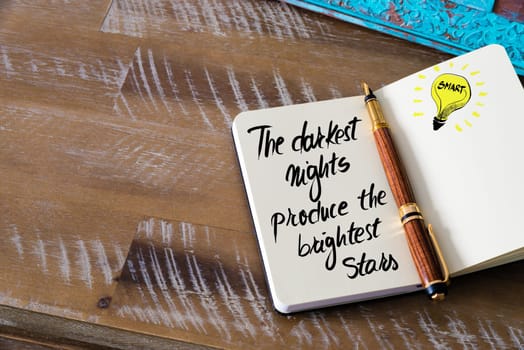 Handwritten text The darkest nights produce the brightest stars with fountain pen on notebook. Concept image with copy space available.