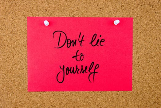 Red paper note with handwritten text Do Not Lie To Yourself pinned on cork board with white thumbtacks