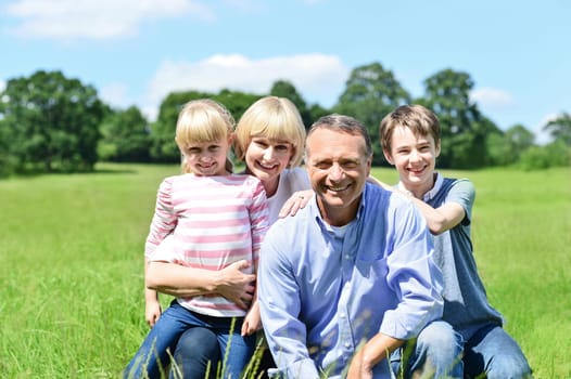 Photo of happy family of four sitting on grass.
