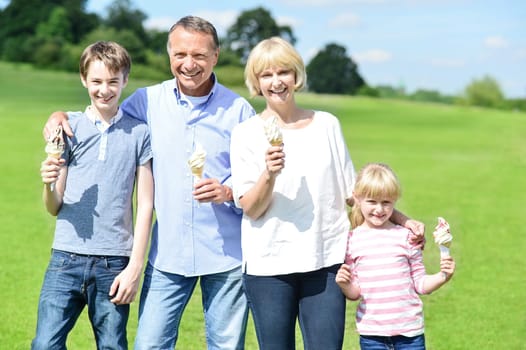 Family standing at grassfield with ice cream and smiling