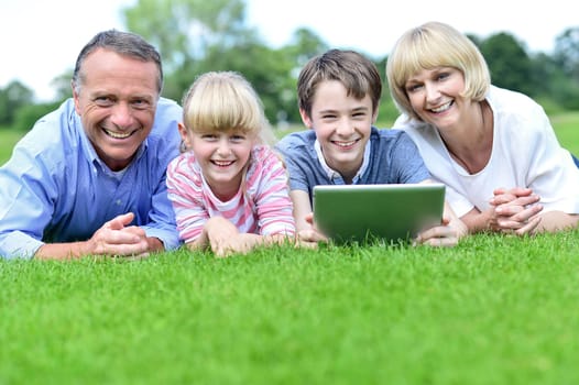 Happy family of four lying in summer park with tablet PC