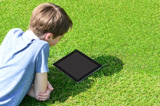 Cute boy lying on grass in park and using tablet pc