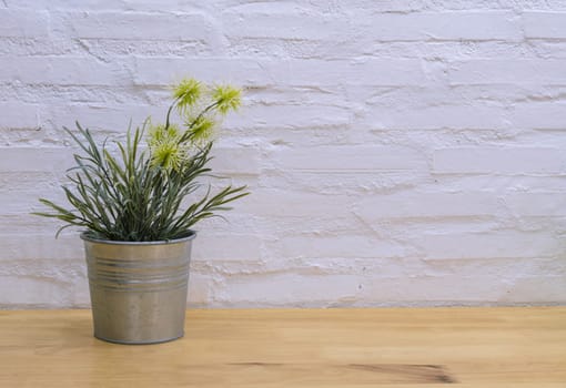 Decorated artificial flowers in flowerpot on wooden table with painted brick wall background