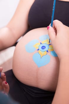 Body art makeup artist painting on the belly of a pregnant young woman