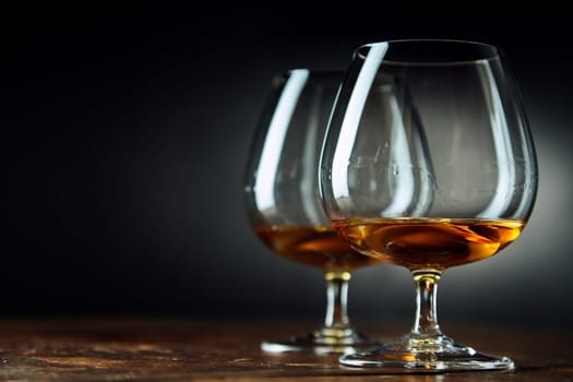 Classic background composed of two goblets filled with bourbon sitting on a wood table in a dark room