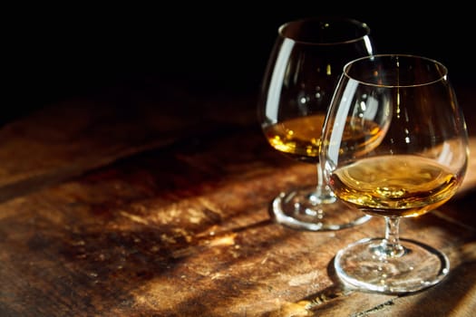 Close up of two bourbon filled glasses on wooden table in a dark room with a few rays of sunlight