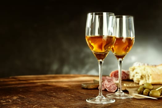 Two glasses of sherry served with tasty traditional Spanish tapas of olives, salami and fresh bread on an old wooden table with copy space