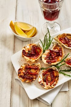 High Angle Still Life View of Platter of Oysters Kilpatrick Prepared with Bacon and Cheese and Served on Painted Wooden Table with Napkin, Lemon Wedges and Goblet of Red Wine