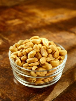 Glass bowl of roasted peanuts or groundnuts for nutritious snacks on a wooden table with copy space, high angle view