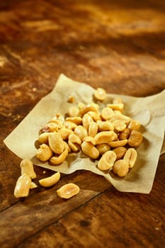 Handful of roasted salted fresh peanuts on a square of crumpled paper on a rustic wooden table with copy space