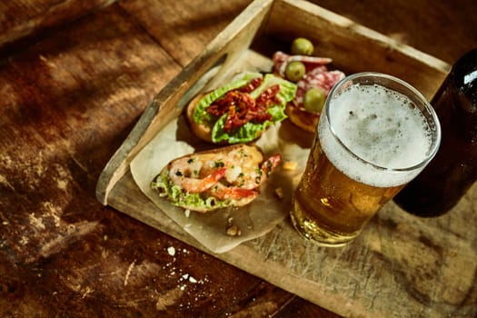 Top down angled view on tapas shrimp and vegetable snacks with tall cup of beer in old wooden serving tray with olives