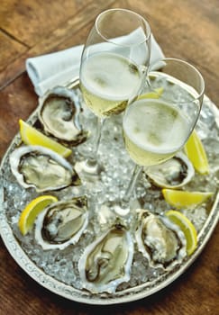 Close up on oysters set up around silver platter filled with crushed ice, lemon slices and champagne glasses in middle