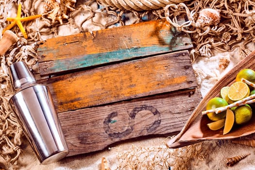 Nautical Themed Background with Copyspace - Cocktail Shaker, Limes and Blank Planks of Weathered Wood on Sand Surrounded by Fishing Net and Seashells