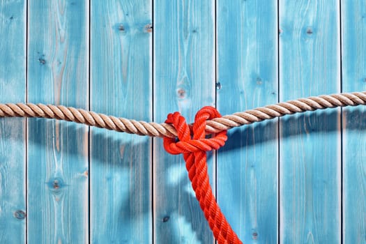 Close Up Still Life of Red Rope Tied Around Natural Fiber Rope Against Blue Painted Wooden Plank Background with Copy Space