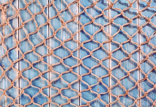 Nautical Themed Background of Natural Fiber Fishing Net Spread Out Across Weathered Blue Painted Wooden Background