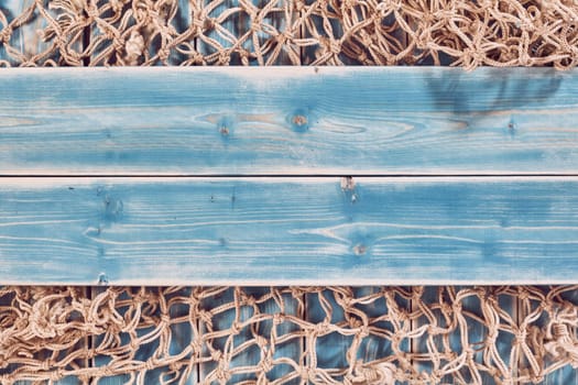 High Angle Still Life of Planks of Blue Painted Wood Horizontal Through Center of Frame and Overlay on Natural Rope Fishing Net - Nautical Themed Background with Copy Space