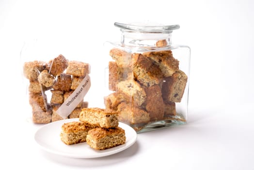 Whole wheat rusks on display in plastic bag, glass bottle and on white plate, on white isolated background.