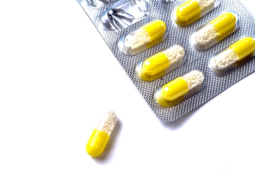 One white and yellow capsule lies in front of an opened and used packet of the same capsules, with six more capsules in the packet.
