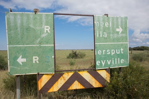 An old deteriorated road sign next to the road with a big rectangular piece in the middle completely missing serve as a frame for the landscape in the background