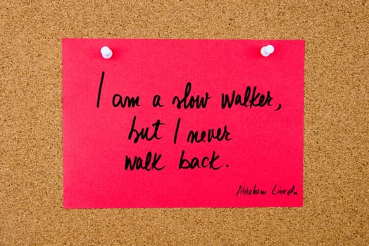 Quote I am a slow walker, but I never walk back by Abraham Lincoln, written on red paper note pinned on cork board with white thumbtacks, copy space available