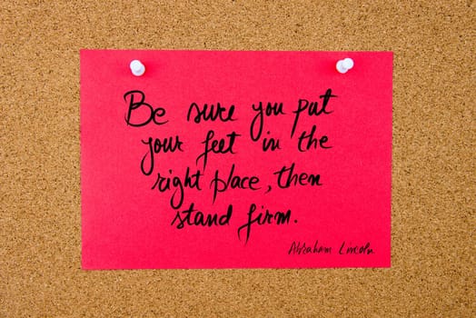 Quote Be Sure You Put Your Feet In The Right Place, Then Stand Firm by Abraham Lincoln, written on red paper note pinned on cork board with white thumbtacks, copy space available