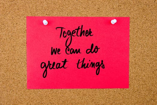 Red paper note with handwritten text Together We Can Do Great Things pinned on cork board with white thumbtacks