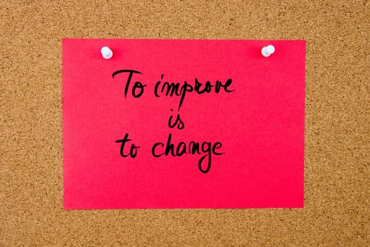 Red paper note with handwritten text To Improve Is To Change pinned on cork board with white thumbtacks