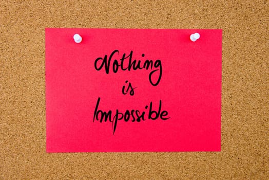 Red paper note with handwritten text Nothing Is Impossible pinned on cork board with white thumbtacks