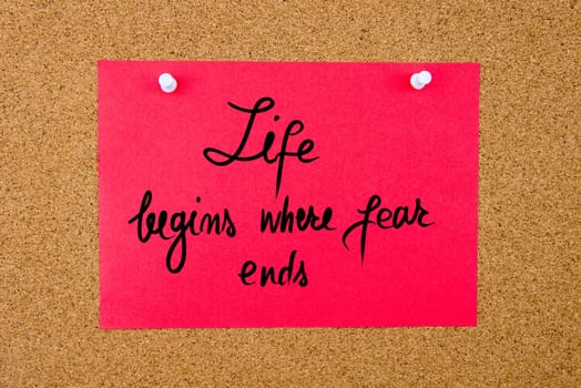 Red paper note with handwritten text Life Begins Where Fear Ends pinned on cork board with white thumbtacks