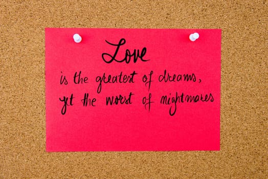 Red paper note with handwritten text Love Is The Greatest Of Dreams Yet The Worst Of Nightmares pinned on cork board with white thumbtacks