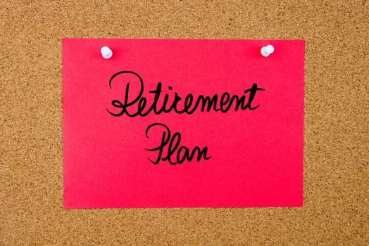 Red paper note with handwritten text Retirement Plan pinned on cork board with white thumbtacks