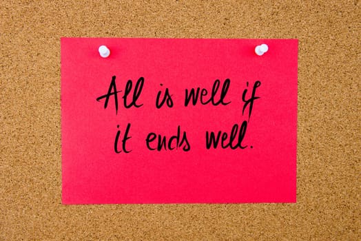 Red paper note with handwritten text All Is Well If It Ends Well pinned on cork board with white thumbtacks