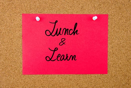 Red paper note with handwritten text Lunch and Learn pinned on cork board with white thumbtacks